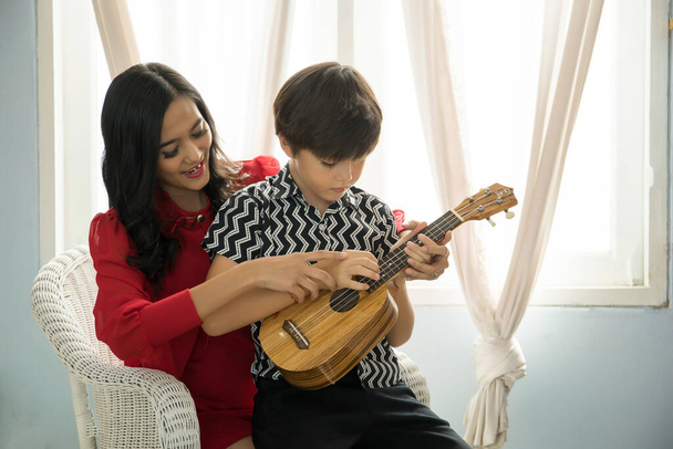 母は息子にリビングでギターの弾き方を教える. - 写真・画像