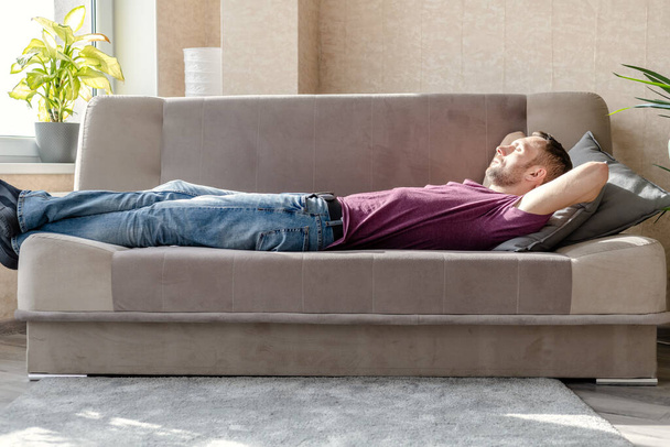 junger Mann liegt auf einem Sofa in einem hellen Raum - Foto, Bild