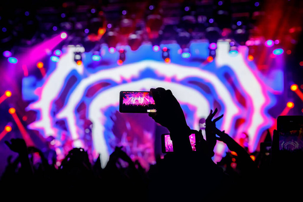 Смартфон в руке на концерте, фиолетовый свет со сцены
. - Фото, изображение