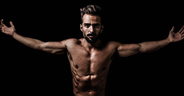 Spaanse jonge fitte en knappe man met open armen en agressief zicht op een zwarte achtergrond. kopieerruimte - Foto, afbeelding