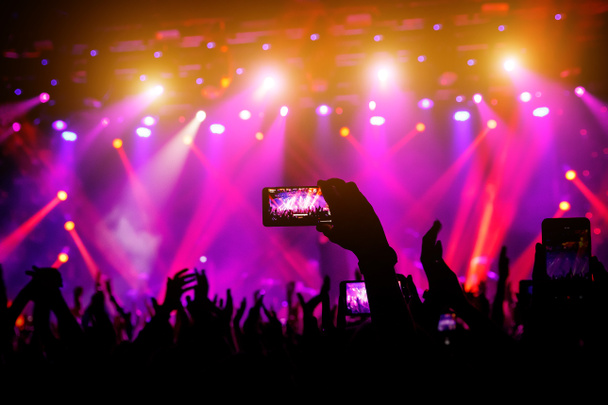 Smartphone στο χέρι σε μια συναυλία, μωβ φως από τη σκηνή. - Φωτογραφία, εικόνα