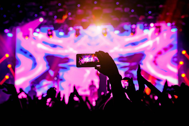 Smartphone en la mano en un concierto, luz púrpura desde el escenario
. - Foto, imagen