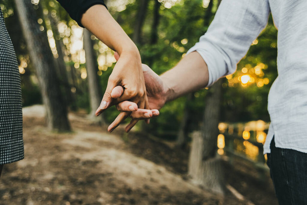 Nahaufnahme der ineinander verschlungenen Hände eines verliebten Paares beim Spaziergang durch einen Wald. - Foto, Bild