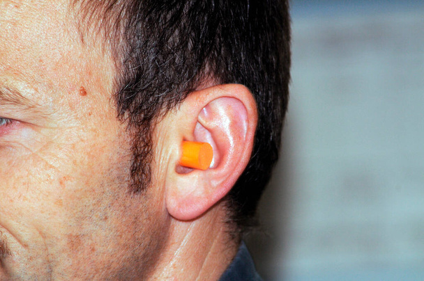 Mann mittleren Alters trägt orangefarbene Ohrstöpsel zum Gehörschutz - Foto, Bild
