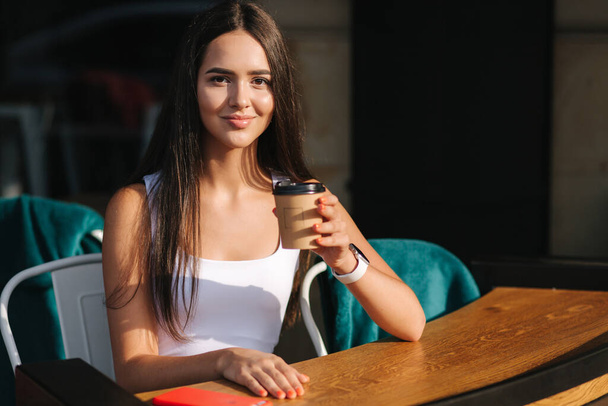 Attractive girl drink coffee on the terrace. Beautiful brunette resting during a break. Social distance - Fotó, kép