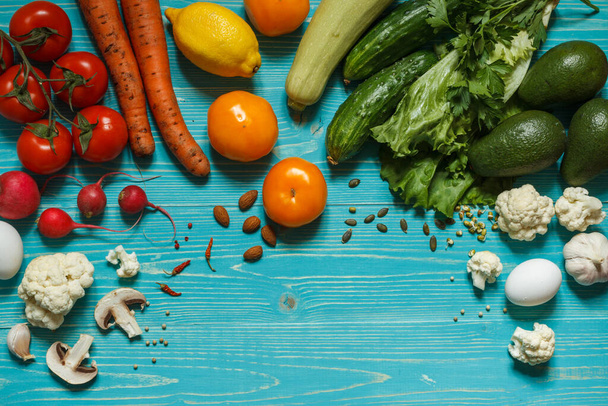 Fresh vegetables, mushrooms, eggs and seeds arranged by color on an aquamarine wooden background with space - Photo, Image