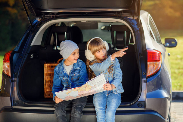 Agreeable boy and girl are looking at the road map while sitting in the autos trunk and discussing the move direction. Family vacation trip by car. - Fotoğraf, Görsel
