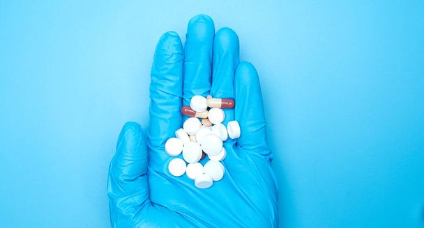 Doctor hand in Medical gloves blue holding Many white pills Antiviral tablets COVID-19 on blue background, Top view Blank for design copy space. - Photo, Image