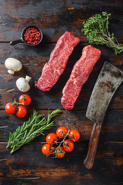 Organic denver steak, raw meat, marbled black angus beef cut on metal butcher cleaver knife with rosemary and farm herbs over old wood table background top view . - Photo, Image