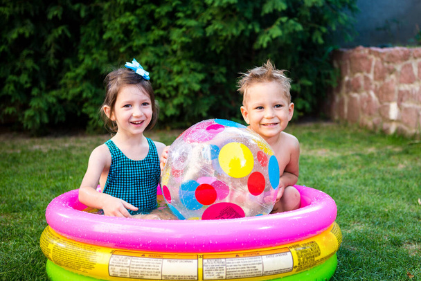 Two children with beach ball at swimming pool. Joyful kid playing in inflatable pool backyard. Little kids at swimming pool on sunny day. Colorful swimming pool ball. Healthy babies summer activity. - Photo, Image