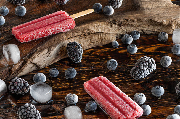 Frozen berries, ice lollies and ice cubes over a wooden board - Photo, Image