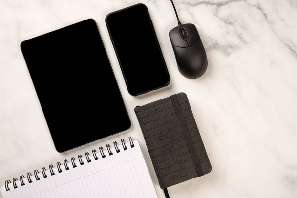 Marmorschreibtisch mit Handy- und Tablet-Attrappe mit Notizbuch, Maus und Terminkalender auf einem Draufsicht-Konzept - Foto, Bild