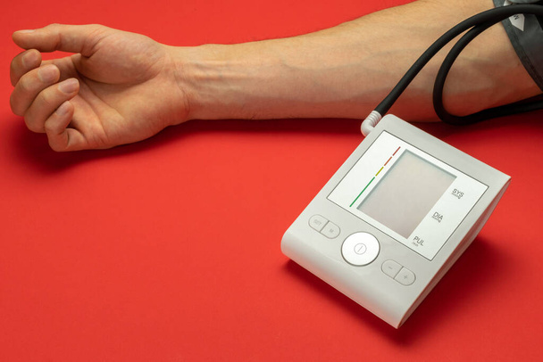 Drukmeter. Hypertensie van de bloeddrukmeter van de patiënt. Gezondheidsmonitor voor controle van de bloeddruk van de arts geïsoleerd op rode achtergrond. Man hand cardio controle. - Foto, afbeelding