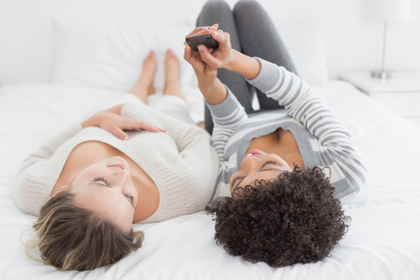 Two relaxed female friends reading text message in bed - Foto, Bild