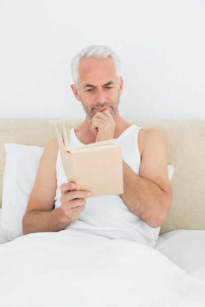 Relaxed mature man reading book in bed - Foto, immagini