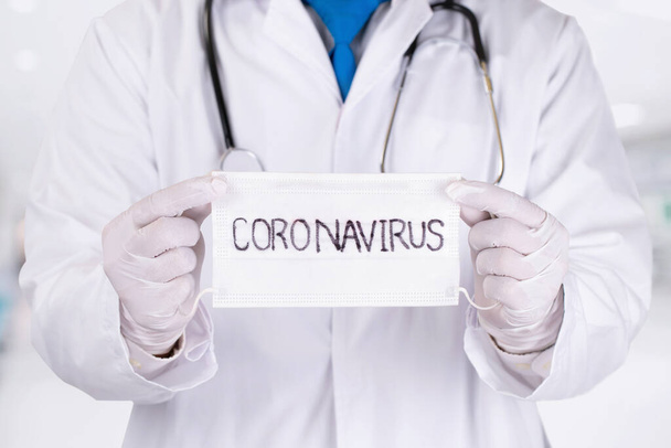 Cierre las manos del médico sosteniendo la máscara quirúrgica con el texto del coronavirus escrito en él. Infección por el virus nCoV 2019 en la ciudad de Wuhan. El Covid-19 (SARS-CoV-2) se extendió por todo el mundo. Impacto del virus pandémico
. - Foto, imagen