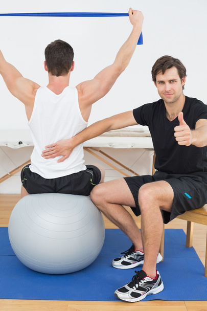 Therapist gestures thumbs up besides man on yoga ball - Foto, Imagem