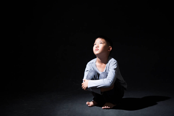 Asian Boy Sitting on Floor and Face Down on knee  ISOLATED on Black Background. Concept : Depressed. Disappointed. Emotion.  - 写真・画像