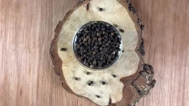 Μαύρο πιπέρι μπιζέλια περιστρέφεται σε ένα γυάλινο πιάτο σε ξύλινο φόντο - Πλάνα, βίντεο