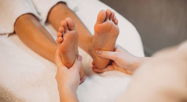 close-up foto van een voeten massage sessie naar een jonge vrouw liggend op de bank in een spa salon - Foto, afbeelding