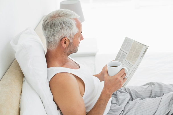 Mature man with coffee cup and newspaper in bed - Photo, Image