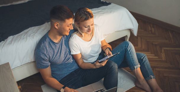 Foto vista dall'alto di una coppia caucasica sdraiata sul pavimento in camera da letto e sorridente allegramente mentre si utilizza un tablet
 - Foto, immagini