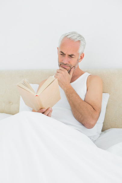 Relaxed mature man reading book in bed - Fotografie, Obrázek