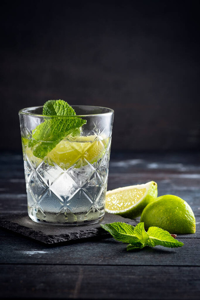 Vodka con agua y hielo en un vaso Copa - cóctel alcohólico con lima y menta
 - Foto, Imagen