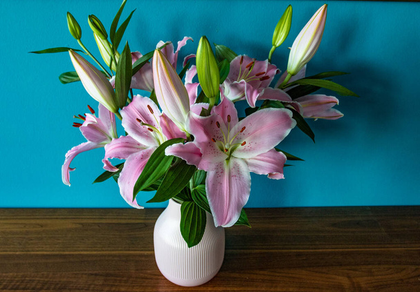 Fialové lilie ve váze jako kytice u modré zdi - Fotografie, Obrázek