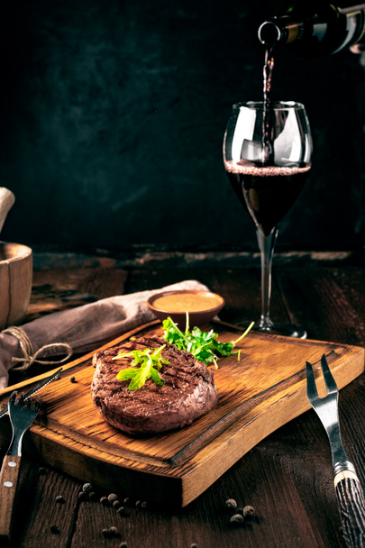 Grillattua naudanlihapihviä, jossa on viiniä, veitsi ja haarukka puulaudalla. Koko paahdettu pala lihaa, maalaismainen tyyli
 - Valokuva, kuva