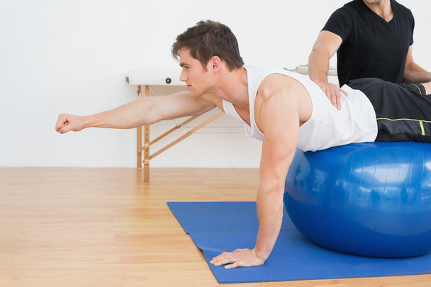 Physical therapist assisting young man with yoga ball - Fotoğraf, Görsel