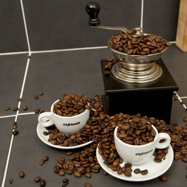 タイル張りのキッチンワーク表面にローストコーヒー豆、エスプレッソカップとグラインダーの静物画 - 写真・画像