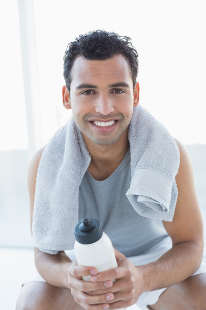 muž s ručníkem kolem krku drží láhev s vodou ve fitness studiu - Fotografie, Obrázek