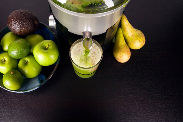 A juicer pouring fruit and vegetable juice into a drinking glass on a kitchen worktop - 写真・画像