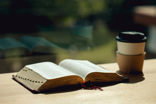 Open book with cup of coffee on wooden desk beside the window - 写真・画像