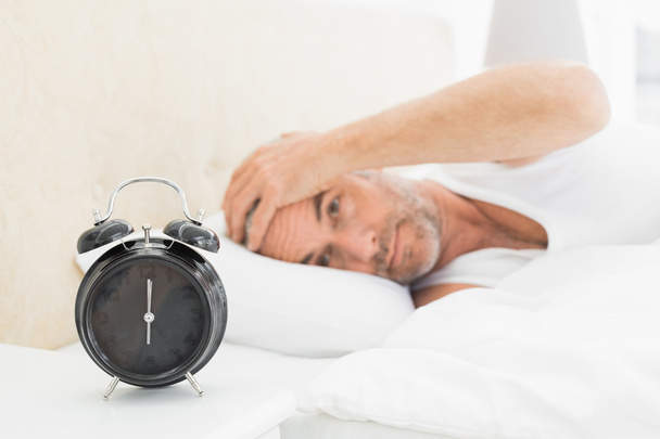 Man resting in bed with alarm clock in foreground - Foto, Imagen