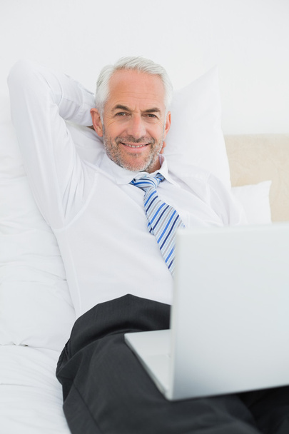 Relaxed mature businessman with laptop in bed - Foto, afbeelding