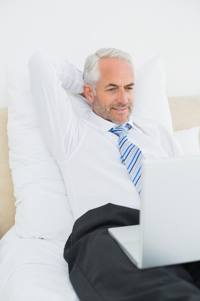 Зрелый бизнесмен смотрит на ноутбук в постели
 - Фото, изображение