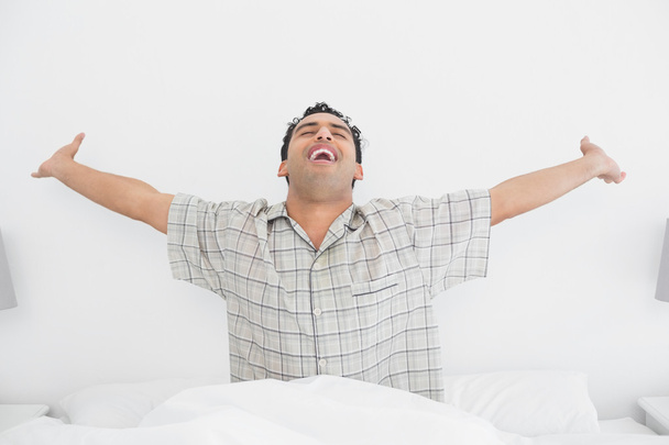 Веселий молодий чоловік розтягує руки в ліжку
 - Фото, зображення
