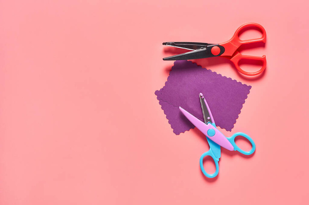 Two scissors for decorative curly cutting and blank paper for craft with wave border on pink background. Concept of handmade, leisure or preschool education - Photo, image