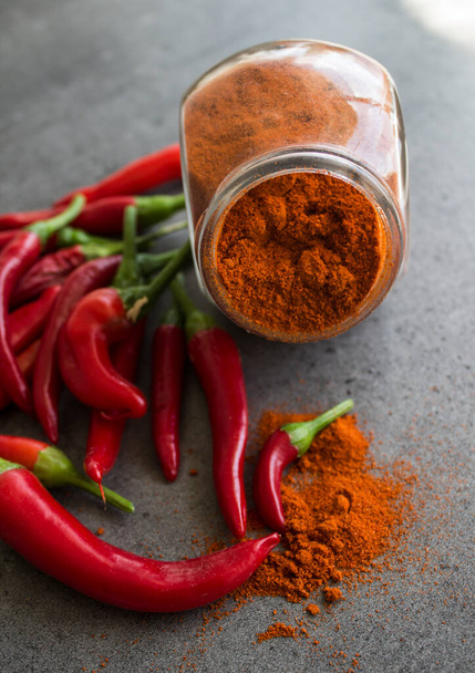 Red chili peppers and paprika powder in glass spice jar on stone table. Dark grey background with copy space. Ingredients top view photo. Vegetable texture close up.  - 写真・画像