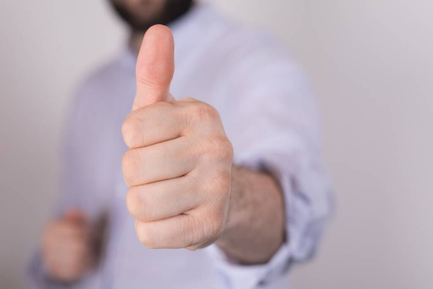 A closeup of a person doing the thumbs-up gesture under the lights on a blurry background - Photo, Image