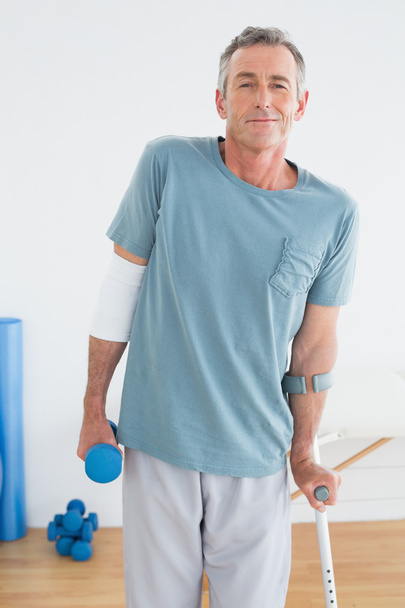 Smiling mature man with crutch and dumbbell - Φωτογραφία, εικόνα
