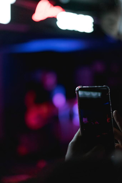 A vertical selective focus shot of hands holding a phone and taking video in the bar - 写真・画像