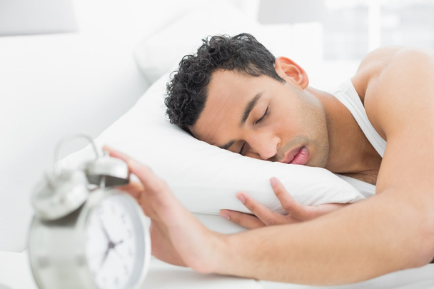 Man in bed extending hand to alarm clock - Photo, Image