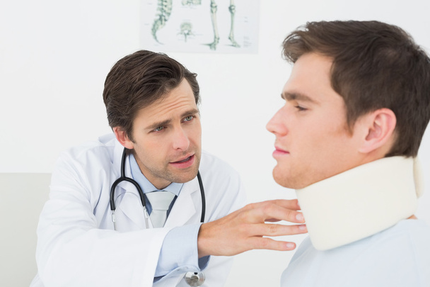 Doctor examining a patients sprained neck at office - Foto, afbeelding