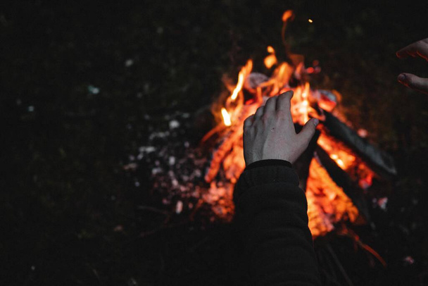 A closeup shot of a person warming his hands on a campfire at night - perfect for wallpapers - Photo, Image
