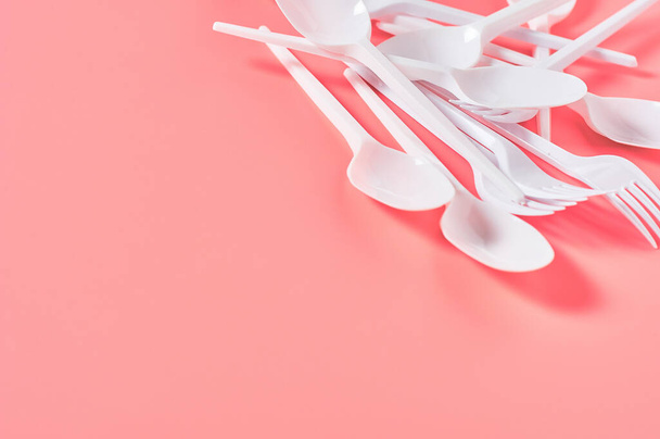 Heap of white disposable spoon and fork on pink background. Concept of save environment, ecology, recreation on picnic, party and other events. Copy space - Фото, зображення