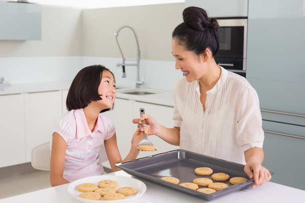 Girl looking at her mother prepare cookies in kitchen - 写真・画像