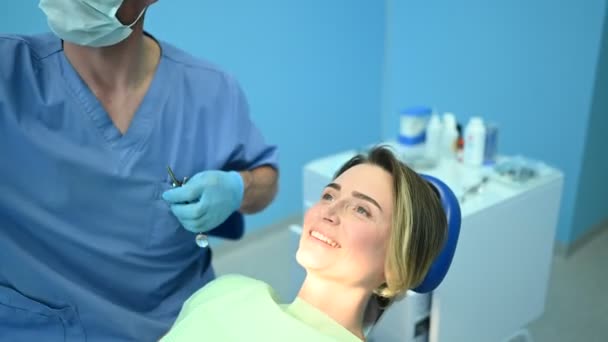Стоматолог осматривает зубы пациента с помощью ложки для отпечатков зубного оборудования в стоматологическом кабинете. Концепция стоматологии и здравоохранения. Доктор в одноразовой медицинской маске для лица, улыбающаяся счастливая женщина
. - Кадры, видео